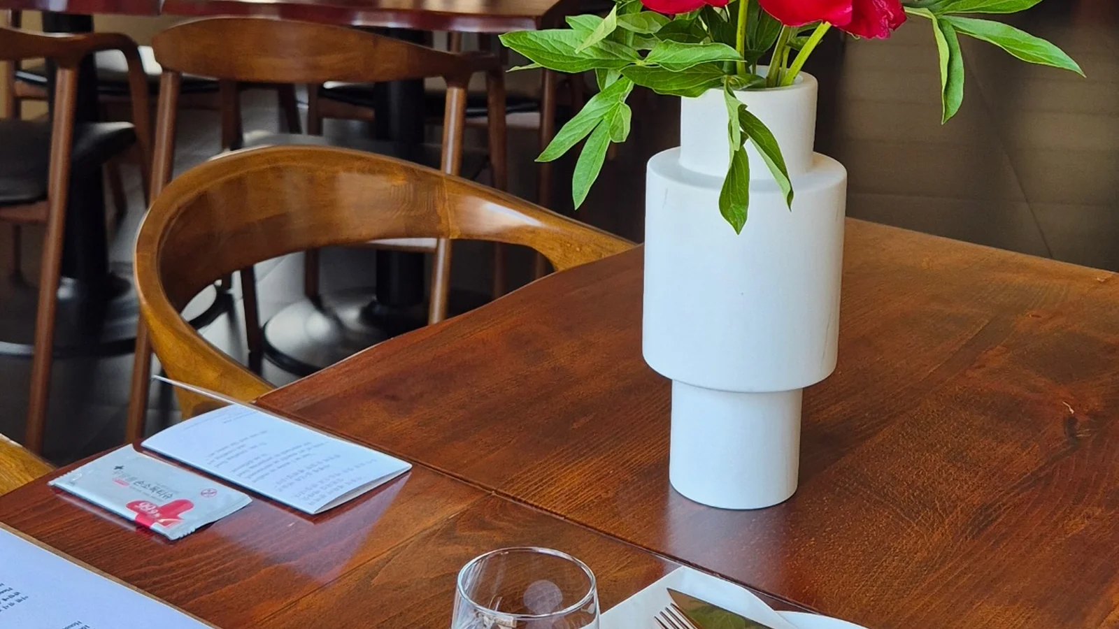 A white vase of red seasonal flowers on a wooden table