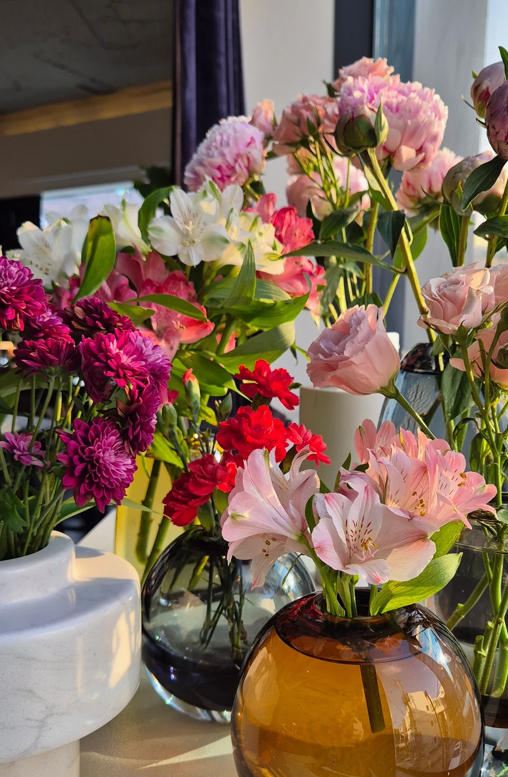 Seasonal flowers in many colours arranged across several vases