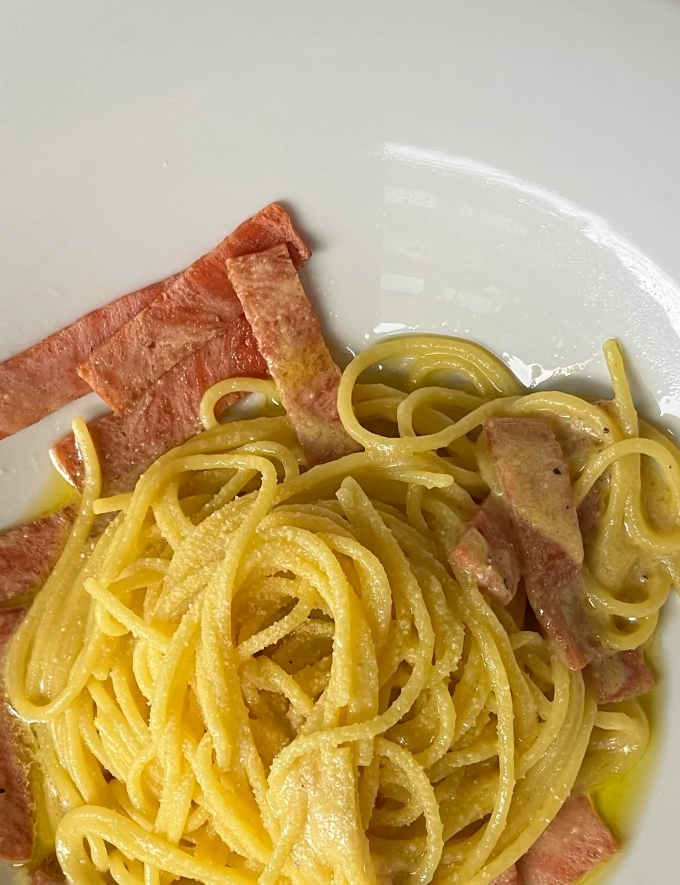 Spaghetti evenly coated with sauce, with vegan bacon