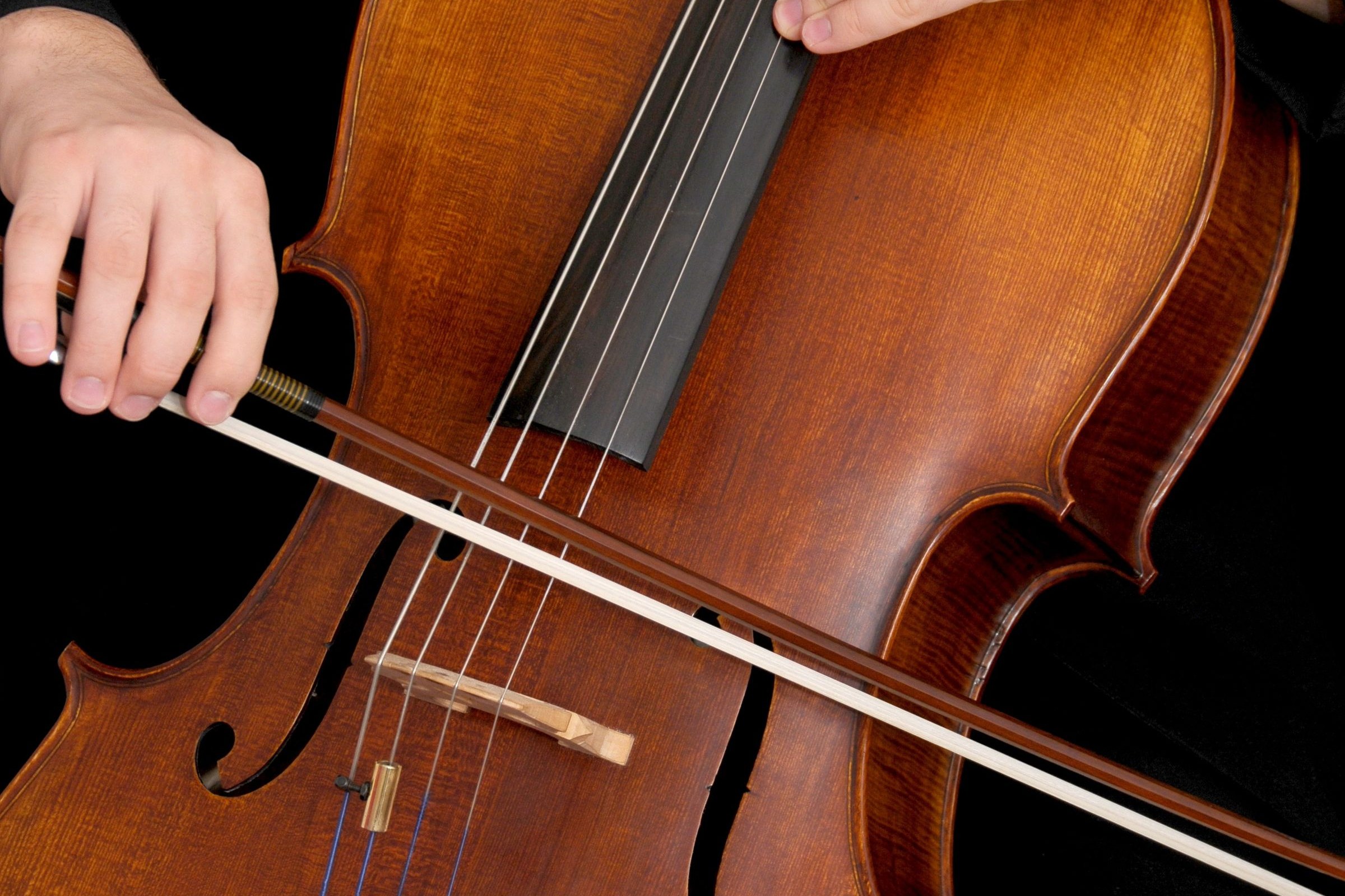 A musician's hand bowing the strings of a cello
