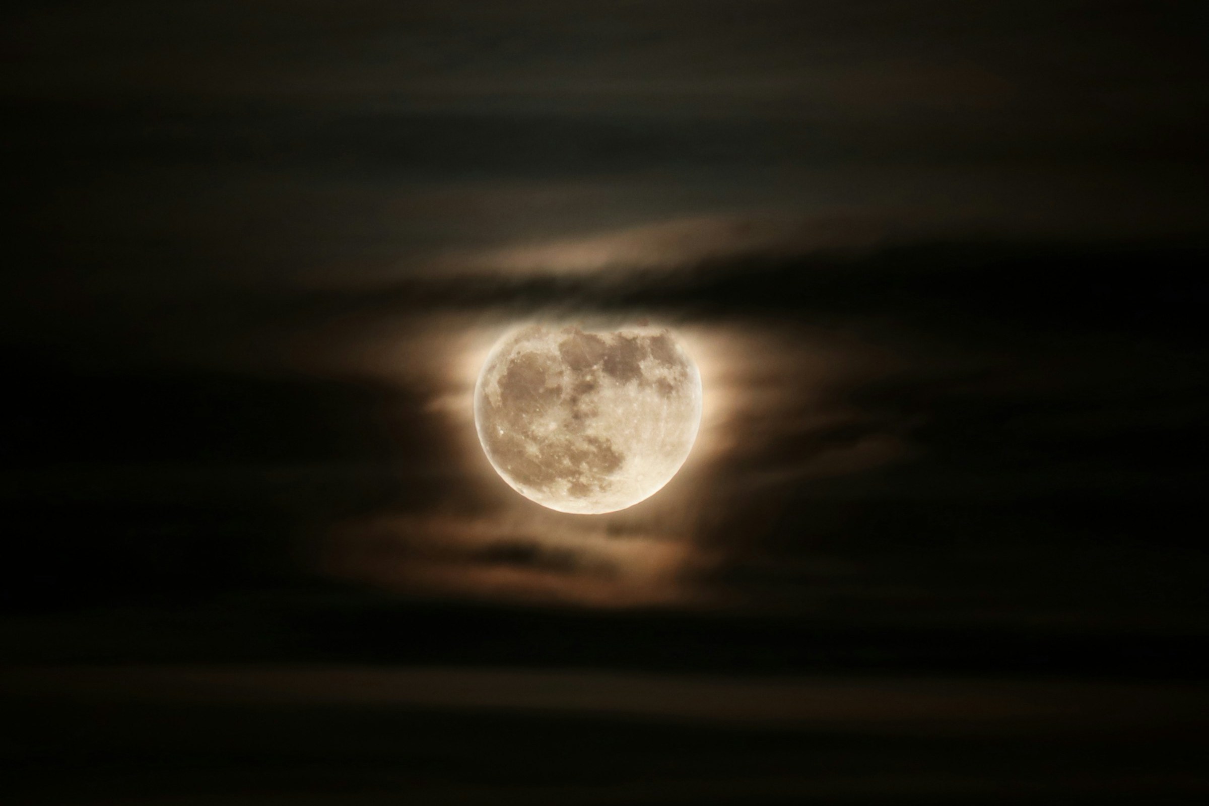 A full moon seen between clouds
