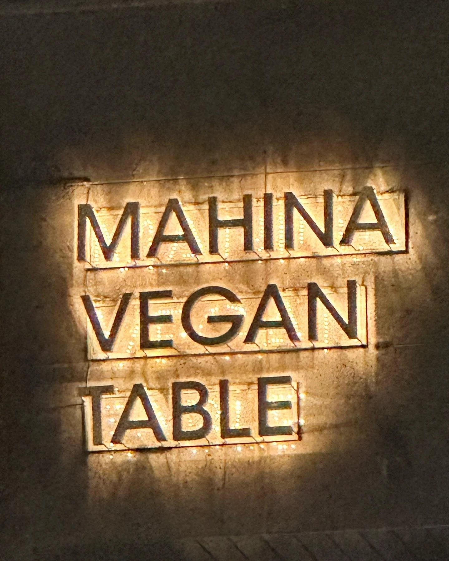Illuminated Mahina Vegan Table sign on the exterior wall at night