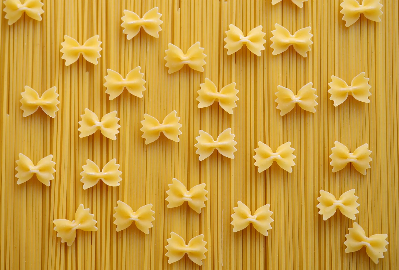 A photograph of farfalle beside long, straight pasta