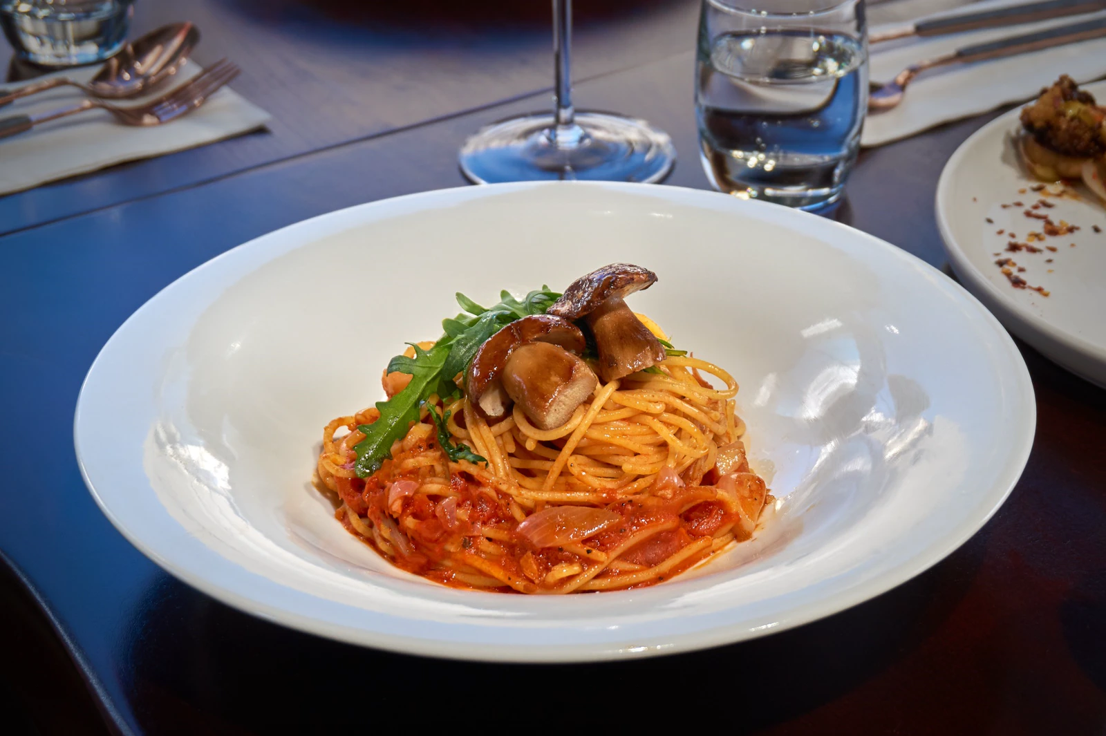 Tomato-sauce pasta topped with mushrooms in a white bowl